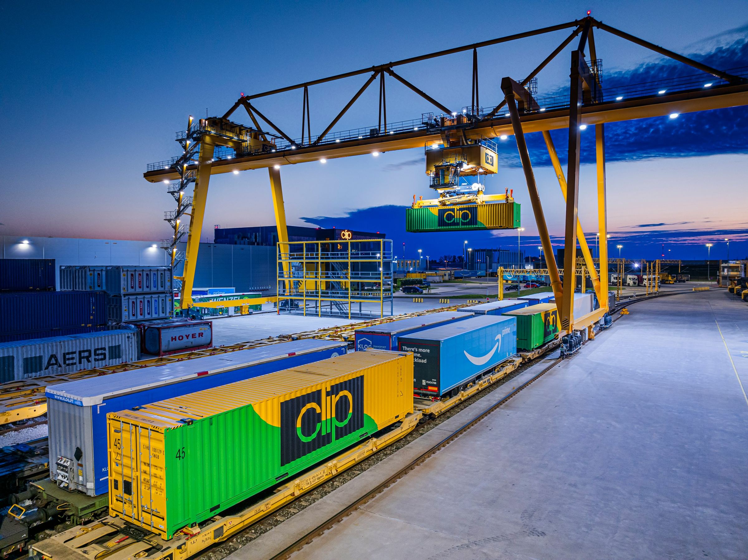 Containers loaded on rail wagons under a gantry crane at dusk