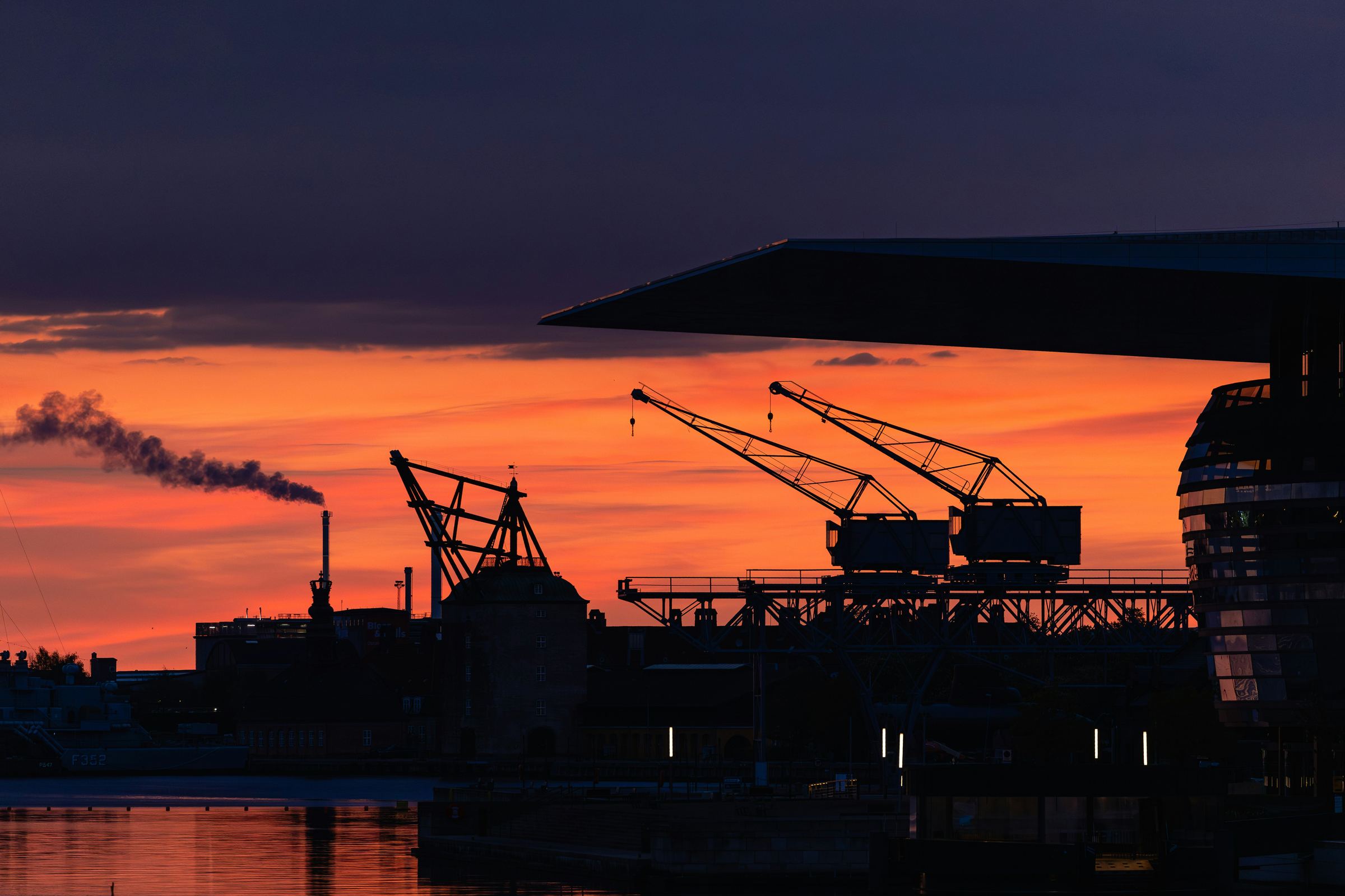 Port cranes and an industrial chimney in silhouette at sunset